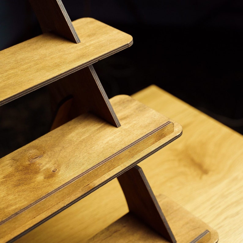 May include: A wooden tiered shelf unit with three shelves. The shelves are made of light brown wood with a dark brown stain. The shelves are angled to create a triangular shape.