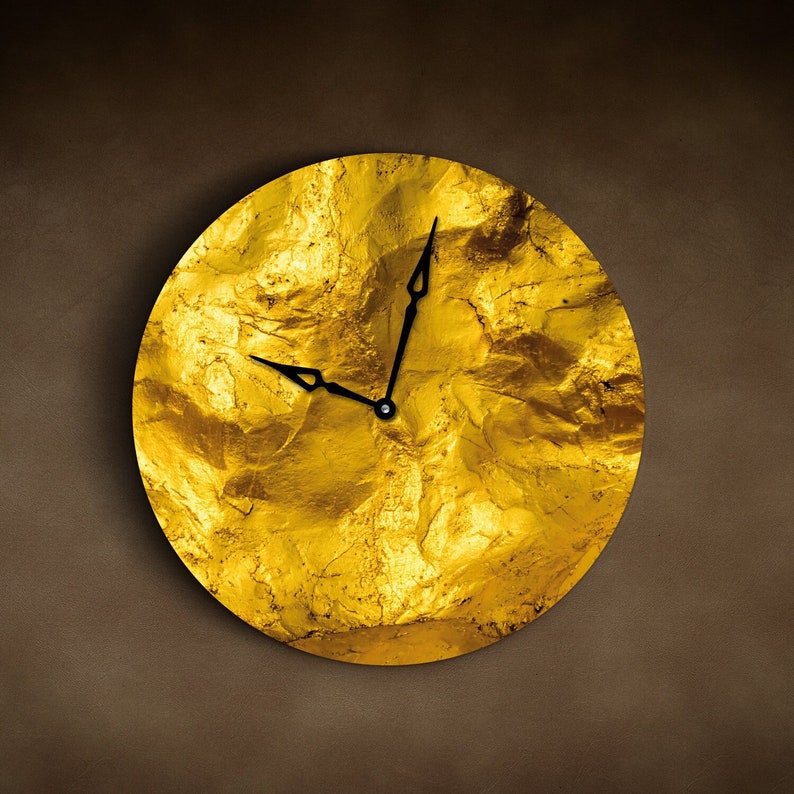 May include: A gold-toned clock with black hands on a textured, gold background. The clock face is round and has a slightly raised edge.
