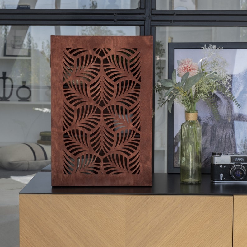 May include: A brown wooden cabinet with a geometric leaf pattern cut out design. The cabinet is sitting on a black surface with a wooden countertop.