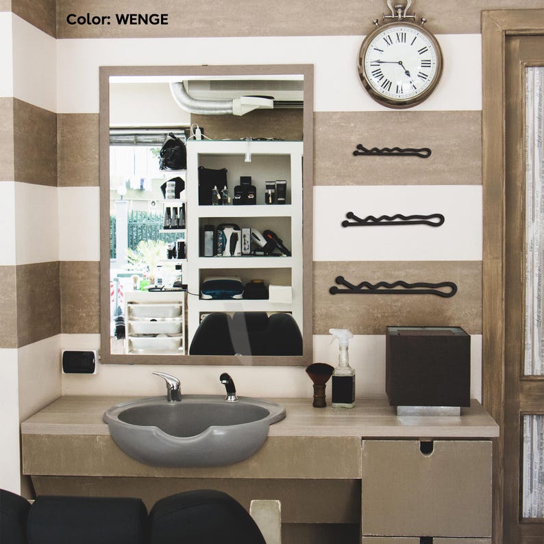 May include: A barber shop interior with a large mirror, a gray sink, and a wall clock. The walls are striped in white and brown. Three black bobby pins are mounted on the wall. The color of the interior is WENGE.