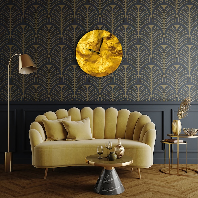 May include: A gold-colored clock with black hands hangs on a wall with a black and gold geometric pattern. A yellow velvet sofa with two pillows sits in front of a coffee table with a black and white marble top.