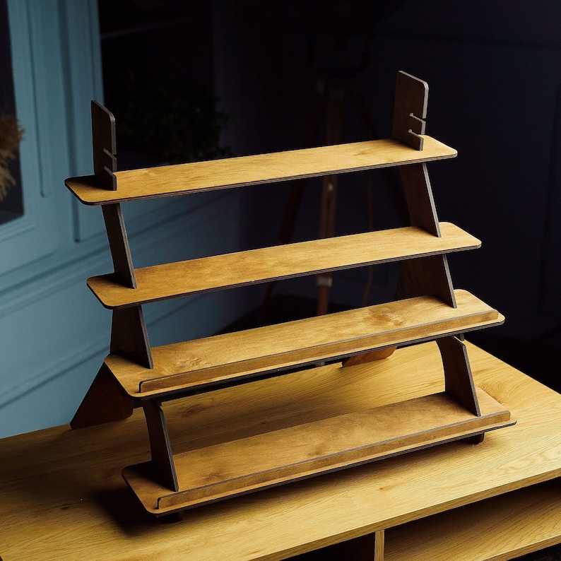 May include: A wooden shelf unit with four shelves. The shelves are made of light brown wood and the frame is made of dark brown wood. The shelf unit is standing on a wooden surface.