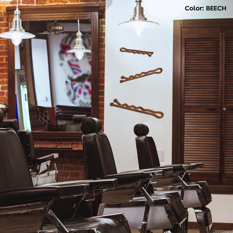 May include: Three beech-colored bobby pins are displayed against a white wall. The bobby pins have a wavy design. The background includes barber chairs, a mirror, and a wooden cabinet. The text "Color: BEECH" is in the upper right corner.