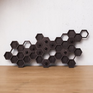 May include: A dark brown wooden wall-mounted honeycomb shelf with several pegs. The shelf is made of interlocking hexagonal shapes, creating a unique and modern design. The pegs are evenly spaced within the honeycomb cells.