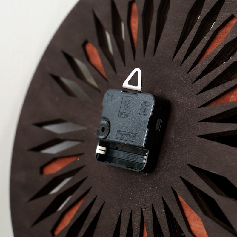 K&ouml;nnte beinhalten: Nahaufnahme der R&uuml;ckseite eines Uhrwerks mit einem schwarzen Kunststoffgeh&auml;use und einem wei&szlig;en dreieckigen Aufh&auml;nghaken. Das Uhrwerk tr&auml;gt die Aufschrift "QUARTZ" und "1988".