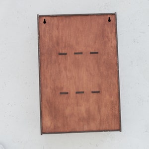 May include: A wooden wall-mounted organizer with six slots for hanging items. The organizer has a dark brown stain and is made of plywood.