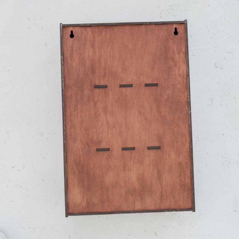 May include: A wooden wall-mounted organizer with six slots for hanging items. The organizer has a dark brown stain and is made of plywood.