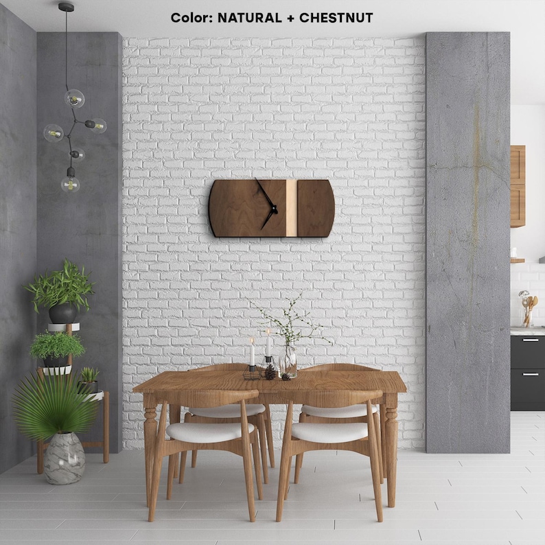 Op de afbeelding: Een houten wandklok met een natuurlijke en kastanjebruine afwerking. De klok heeft een zwarte wijzerplaat met zwarte wijzers en een witte streep in het midden. De klok hangt aan een witte bakstenen muur in een eetkamer.
