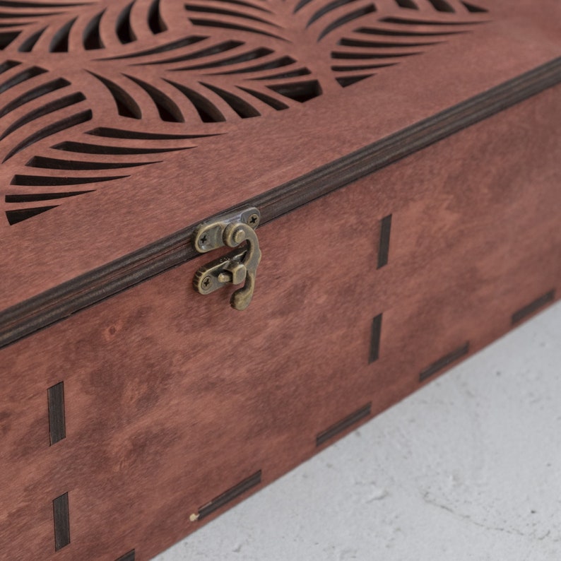 May include: A wooden box with a decorative cutout design on the lid. The box has a brown stain finish and a brass latch.