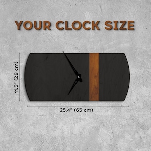 Op de afbeelding: Een zwarte en bruine houten klok met een houtnerfdesign. De klok is 29 cm hoog en 65 cm breed.