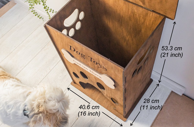 May include: A wooden dog toy storage box with paw-shaped cutouts and the words "Dog Toys" and "Custom Name". The box is 21 inches tall, 16 inches wide, and 11 inches deep. The box is brown.
