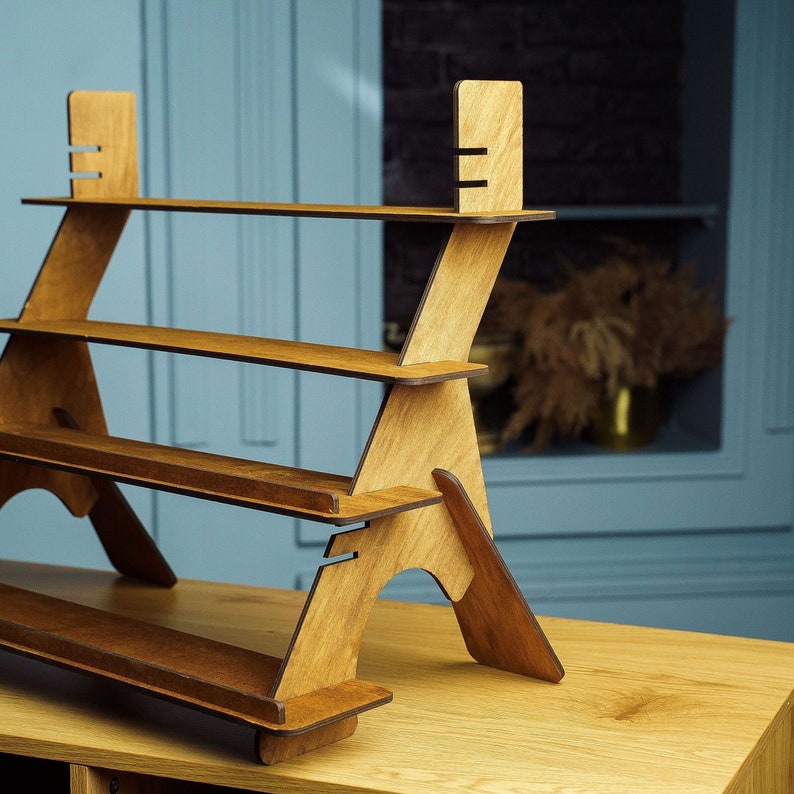 May include: A three-tiered wooden display stand with a natural wood finish. The stand is made of plywood and has a simple, modern design.