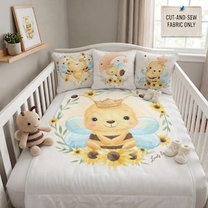 Peut inclure: Un ensemble de literie pour berceau blanc avec une illustration centrale d'une abeille portant une couronne, entourée de tournesols et d'ailes bleu clair. Trois coussins carrés présentent des motifs d'abeilles. Un jouet abeille et des chaussons.