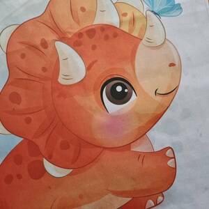 May include: A cartoon illustration of a friendly triceratops in shades of orange and tan, with white horns and a blue butterfly. The dinosaur has a large, expressive eye and a gentle smile, set against a light blue background.