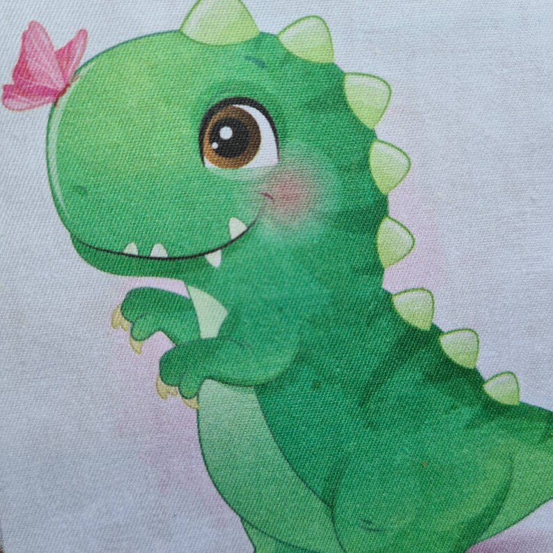 May include: A green cartoon dinosaur with a friendly expression and large brown eyes. A pink butterfly rests on its head. The dinosaur has a row of green spikes down its back and is set against a light background.