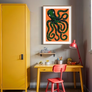 May include: A green octopus with white spots is illustrated on an orange background. The illustration is framed and hanging on a wall in a room with a yellow desk and chair.