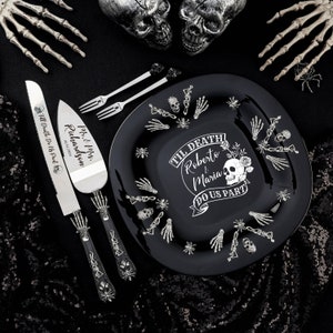 May include: A black ceramic cake plate with a white skull and crossbones design. The plate says "Til Death Do Us Part" with the names Roberto and Maria. The plate is surrounded by silver skeleton hands and spiders.