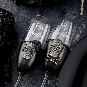 May include: Two black champagne flutes with skull and rhinestone embellishments. The flutes are engraved with "Mrs. Bentley" and "Mr. Bentley".