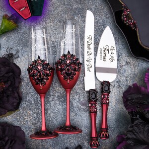 May include: Two red wine glasses with black rhinestone embellishments and the names "Anna & Steven" engraved on them. A red and black cake knife with the text "Mr. & Mrs. Thomas 09/03/2023 Til Death Do Us Part" engraved on it.