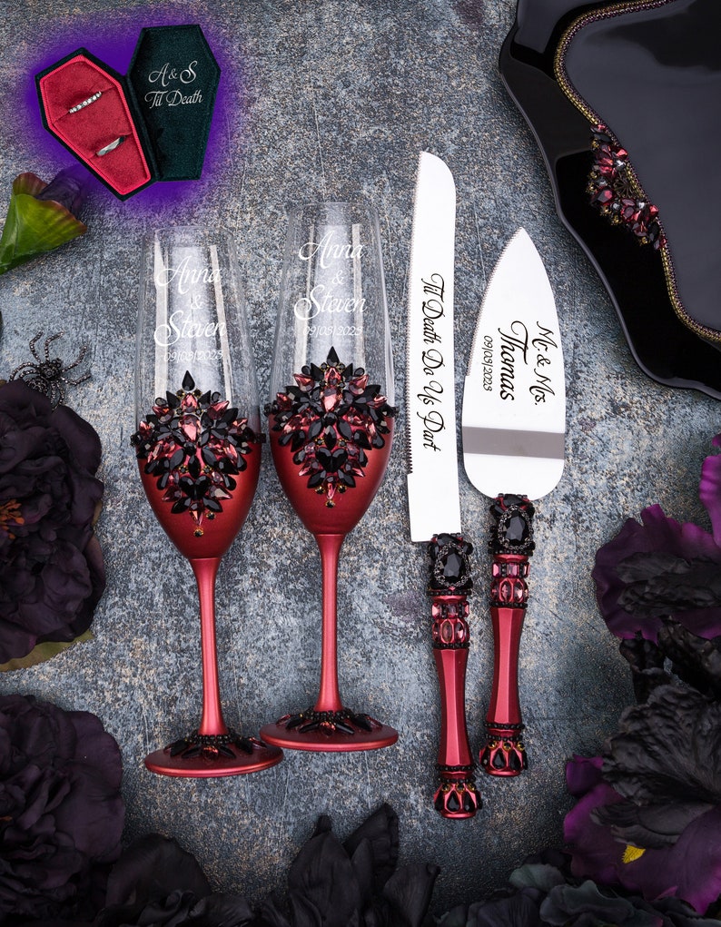 May include: Two red wine glasses with black rhinestone embellishments and the names "Anna & Steven" engraved on them. A red and black cake knife with the text "Mr. & Mrs. Thomas 09/03/2023 Til Death Do Us Part" engraved on it.