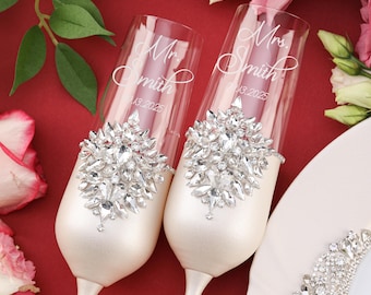May include: Two clear glass champagne flutes with a pearlescent white base. Each flute features a large, silver-toned brooch with clear crystals. The glass is etched with the text Mr. Smith 9.13.2025 and Mrs. Smith 9.13.2025 in white script.