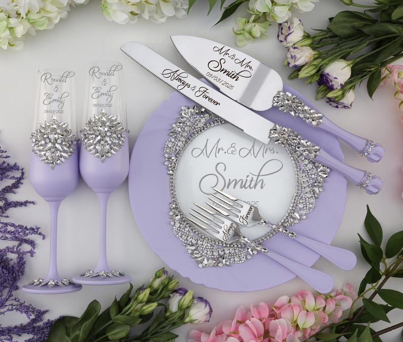 May include: A lavender wedding cake serving set with a knife, two forks, and two champagne flutes. The knife and forks have silver handles with rhinestones and the flutes have silver bands with rhinestones. The cake plate is lavender with a silver rhinestone border and the text "Mr. & Mrs. Smith" in the center.