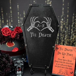 May include: Black coffin-shaped guest book alternative with the text "Til Death" and skeleton hands forming a heart. Includes a sign that says "Til Death Do Us Part". A gothic wedding theme.