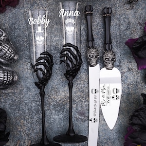 May include: A wedding cake cutting set with a black skeleton hand design. The set includes two champagne flutes with the names "Bobby" and "Anna" etched on them and a cake knife with the text "Till Death Do Us Part! Mr. & Mrs. Williams EST. 2022".