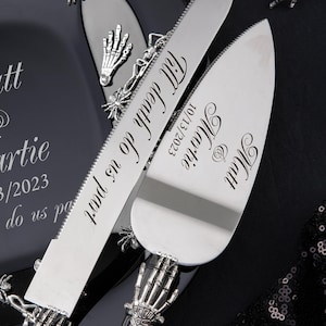 May include: A black and silver wedding cake knife and server set with skeleton hand handles. The knife is engraved with "Till Death Do Us Part" and the date "10/13/2023". The server is engraved with "Mr. & Mrs.  Martie" and the date "10/13/2023".