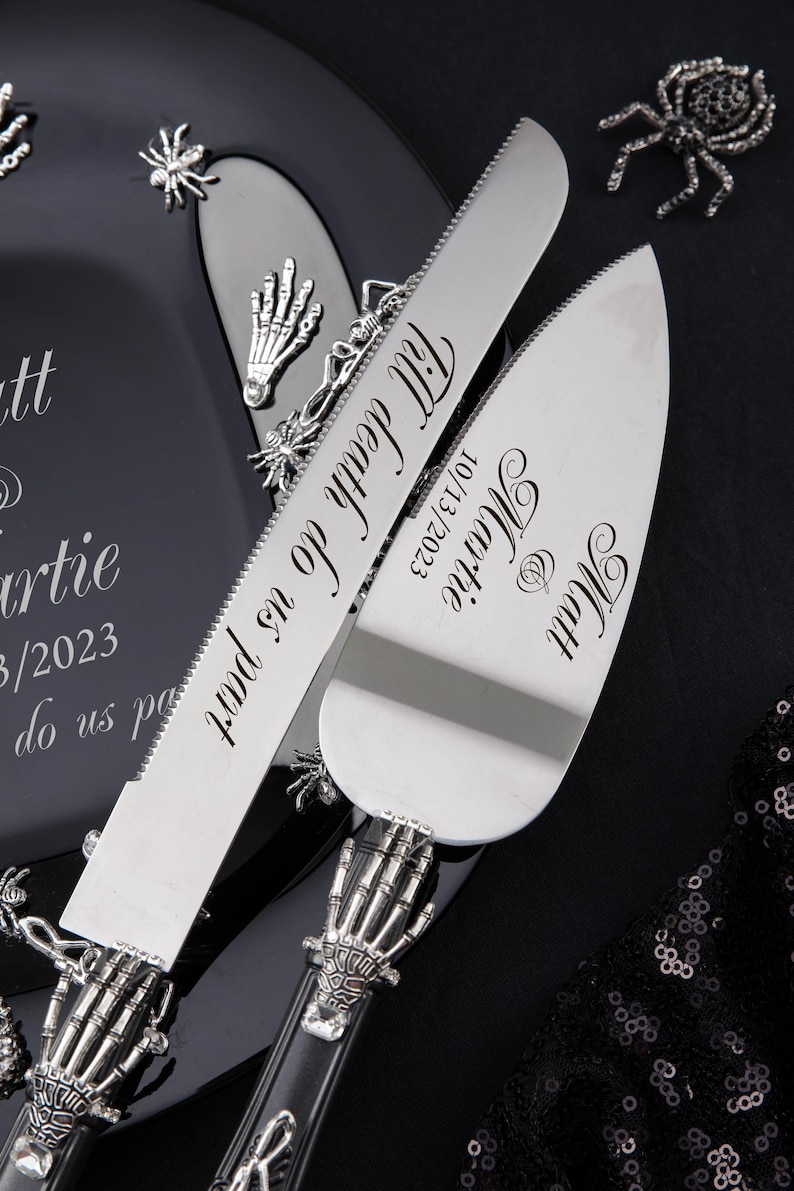 May include: A black and silver wedding cake knife and server set with skeleton hand handles. The knife is engraved with "Till Death Do Us Part" and the date "10/13/2023". The server is engraved with "Mr. & Mrs.  Martie" and the date "10/13/2023".