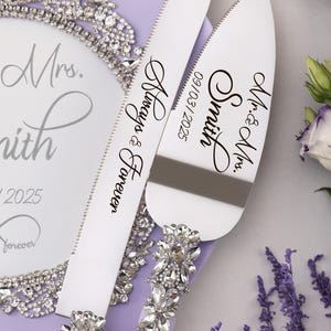 May include: A set of two silver cake cutting knives with purple handles and rhinestone embellishments. The knives are engraved with the text "Mr. & Mrs. Smith 09/03/2025" and "Always & Forever".