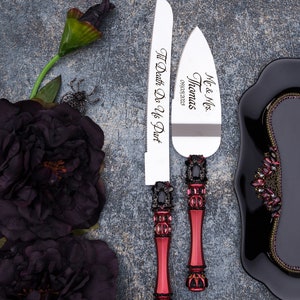 May include: A set of two silver cake knives with black and red jeweled handles. The knives are engraved with "Mr. & Mrs. Thomas 09/10/2023" and "Til Death Do Us Part".