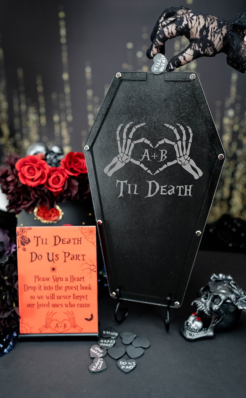 May include: Black coffin-shaped guest book alternative with the text "Til Death Do Us Part" and skeleton hands forming a heart. Includes a sign, heart-shaped tokens, and a skull. A heart token is being dropped into the coffin.