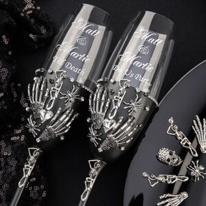 May include: Two black champagne flutes with silver skeleton hands, spiders, and rhinestones. The flutes are engraved with the text "Matt & Martie Till Death" and "Matt & Martie Do Us Part".