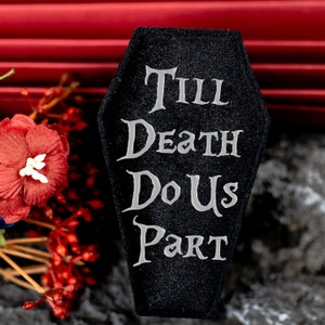 May include: Black velvet coffin-shaped sign with the text "Till Death Do Us Part" in white lettering.