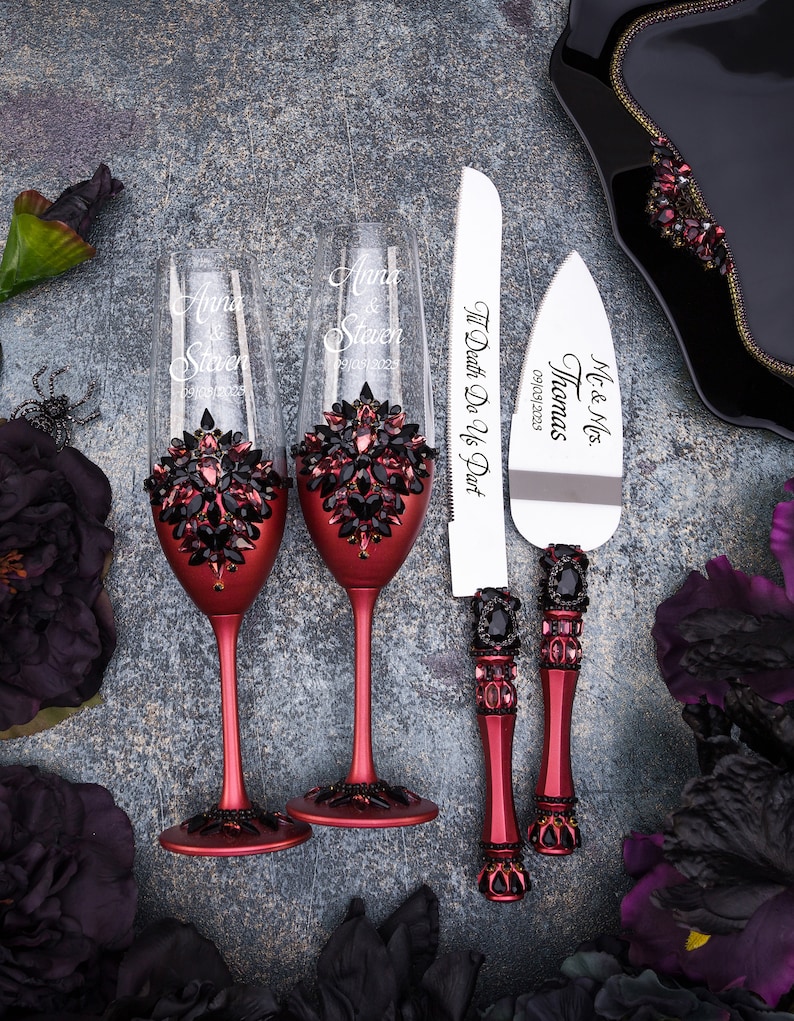 May include: Two red wine glasses with black rhinestone embellishments and the names "Anna & Steven" engraved on them. A red and black cake knife with the text "Mr. & Mrs. Thomas" and "Til Death Do Us Part" engraved on it.