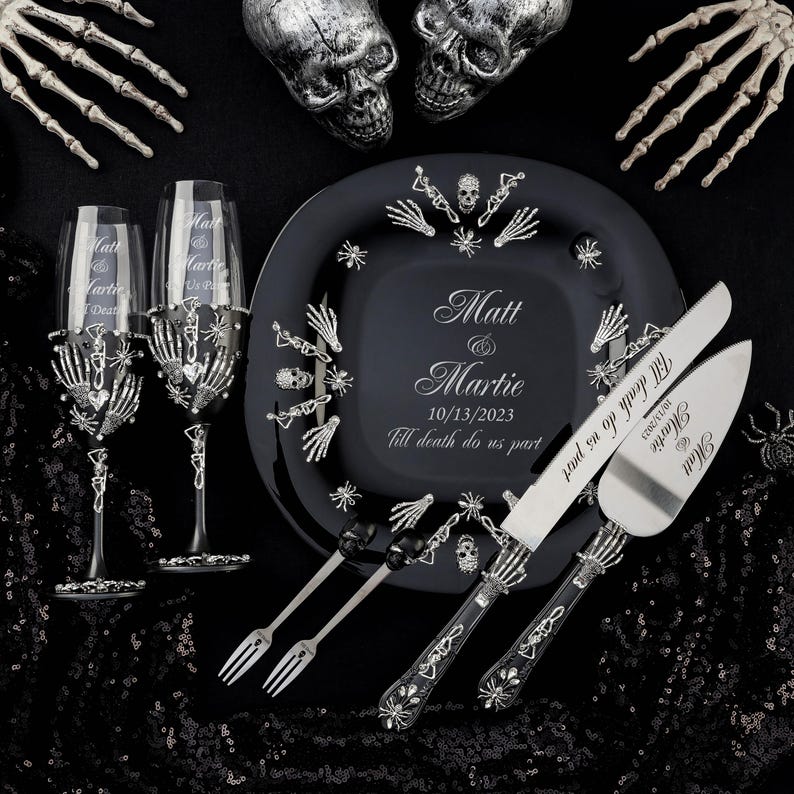 May include: Black and silver wedding cake serving set with a skull and crossbones design. The cake knife and server have the text "Till death do us part" and the date "10/13/2023". The set also includes two black and silver glasses with a skull and crossbones design.
