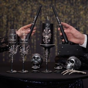 May include: Black wedding candle set with a skull and bone design. The candle is decorated with silver glitter and the words "Matt & Marie" are written on the side. Two black champagne flutes with silver glitter and the words "Till Death" and "Do Us Part" are also included.
