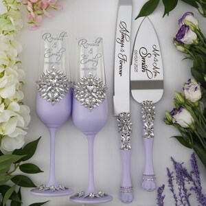 May include: A wedding set with two lavender colored champagne flutes and a cake knife and server. The flutes and handles of the knife and server are decorated with rhinestones. The flutes are engraved with the names "Ronald & Emily" and the date "09/03/2025". The knife is engraved with "Mr. & Mrs. Smith" and the server is engraved with "Always & Forever" and the date "09/03/2025".