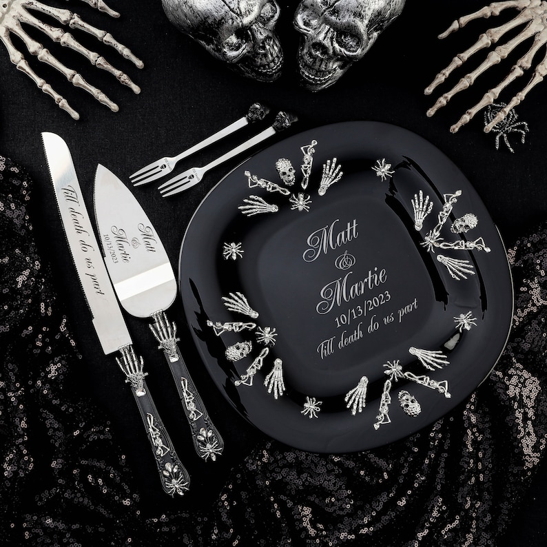 Op de afbeelding: Zwarte en zilveren huwelijkscake mes en server set met skelet handgrepen. Het mes heeft de tekst "Till death do us part" en de datum "10/13/2023". De server heeft de namen "Matt & Martie" en de datum "10/13/2023".
