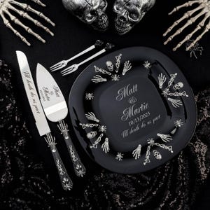 May include: A black glass cake plate with a silver skeleton hand design and the names Matt and Martie, the date 10/13/2023, and the phrase "Till death do us part" engraved on the plate. A silver cake knife and server with skeleton hand handles and the same text engraved on the blades.
