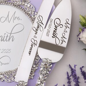 May include: A set of two silver cake cutting knives with purple handles and rhinestone embellishments. The knives are engraved with the text "Mr. & Mrs. Smith 09/03/2025" and "Always & Forever".