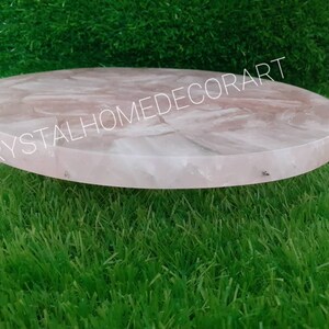 May include: A round, pink, rose quartz serving tray with a smooth, polished surface. The tray is made of natural stone and has a unique, organic shape.