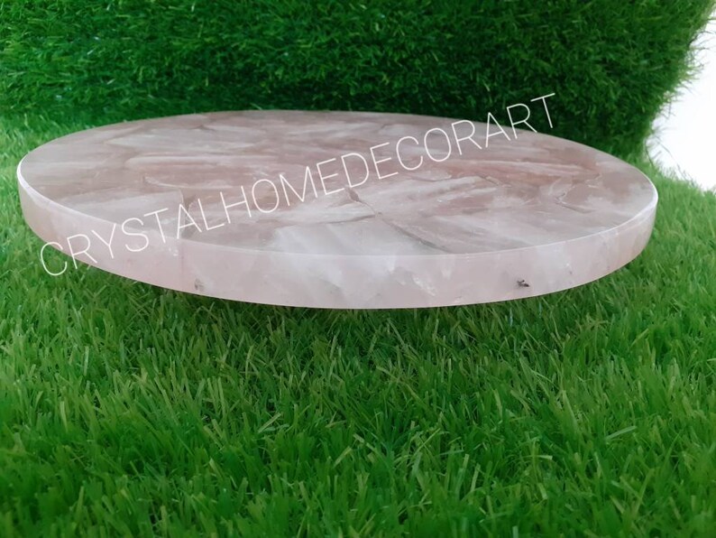 May include: A round, pink, rose quartz serving tray with a smooth, polished surface. The tray is made of natural stone and has a unique, organic shape.