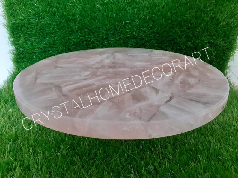 May include: A round, pink, rose quartz serving tray with a polished, smooth surface. The tray is made of natural stone and has a unique, organic pattern.