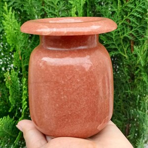 Puede incluir: Un pequeño jarrón de piedra redondo, de color rojo-naranja, pulido, con un borde ancho y plano.