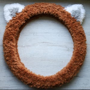May include: Brown fuzzy steering wheel cover with two gray fuzzy ears on top.