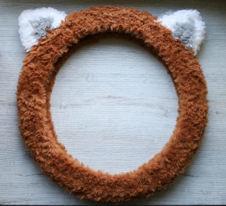 May include: Brown fuzzy steering wheel cover with two gray fuzzy ears on top.