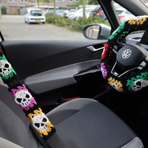 Könnte beinhalten: Ein schwarzer Lenkradbezug mit einem bunten Totenkopf-Muster. Der Bezug ist gehäkelt und besteht aus rotem, grünem, gelbem, rosa und weißem Garn.