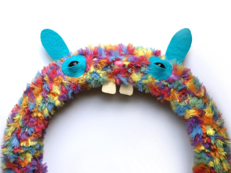 Puede incluir: Una corona circular cubierta de piel sint&eacute;tica esponjosa y multicolor en tonos naranja, amarillo, azul, morado y rojo. Presenta dos orejas de fieltro de color turquesa brillante, dos parches oculares turquesas con pupilas negras, una peque&ntilde;a nariz rosa y dos dientes blancos.